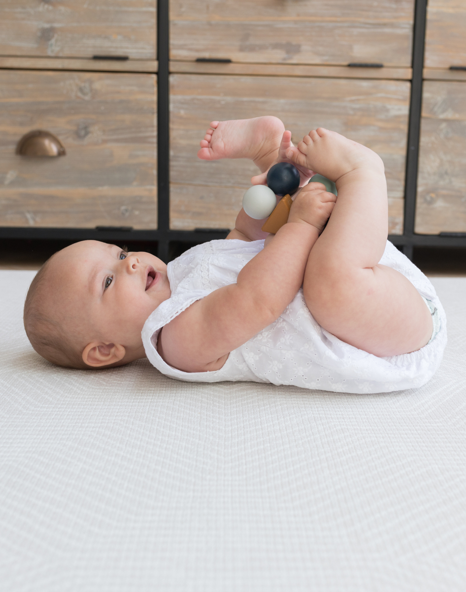 Baby laying on back on neutral play mat with aged kilim design for a ruglike effect comfortable and cushioned on the memory foam while playing with a wooden toy