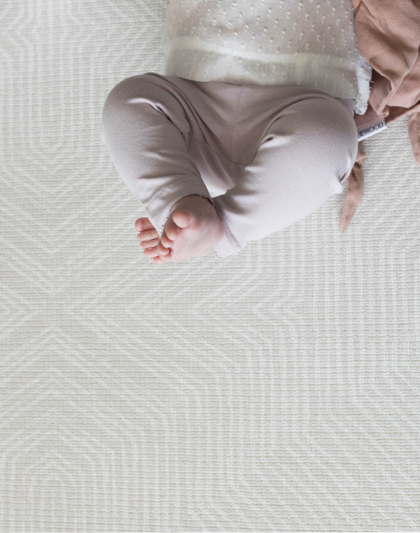 Little feet are pointing up into the air while a baby relaxes on the near neutral play mat with a subtle kilim design 