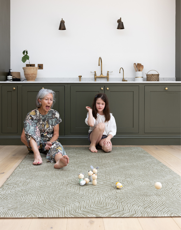 Grandmother and child sit on a large kitchen mat that has a modern kilim textile design to complement the interior 