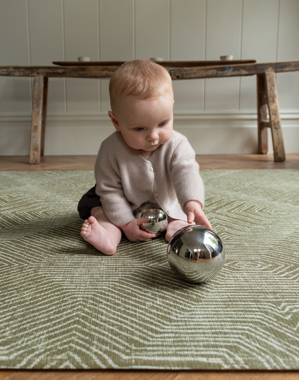 Baby engaged in shiny sensory toys sitting comfortably on green play mat with beautiful kilim textile motif 