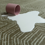 Cup of milk spills on green baby play mat with a sealed surface to make cleaning easier 