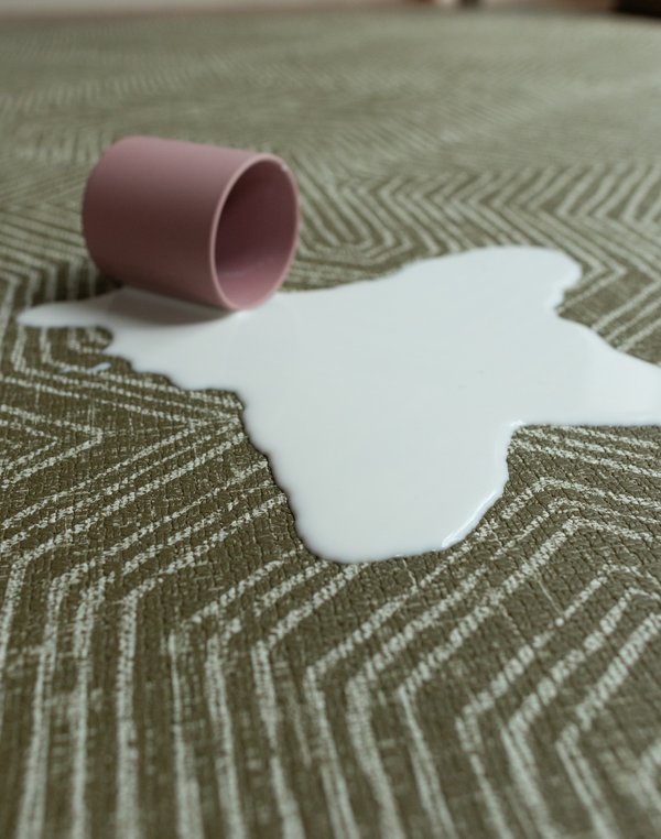 Cup of milk spills on green baby play mat with a sealed surface to make cleaning easier 
