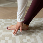 A lady does yoga on The Holbein, a textured baby playmat with a handwoven style and earthy calming tones.