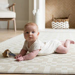 Baby on The Holbein, a calming colour playmat with a Portcullis motif in stone and chalk for tummy time and play.