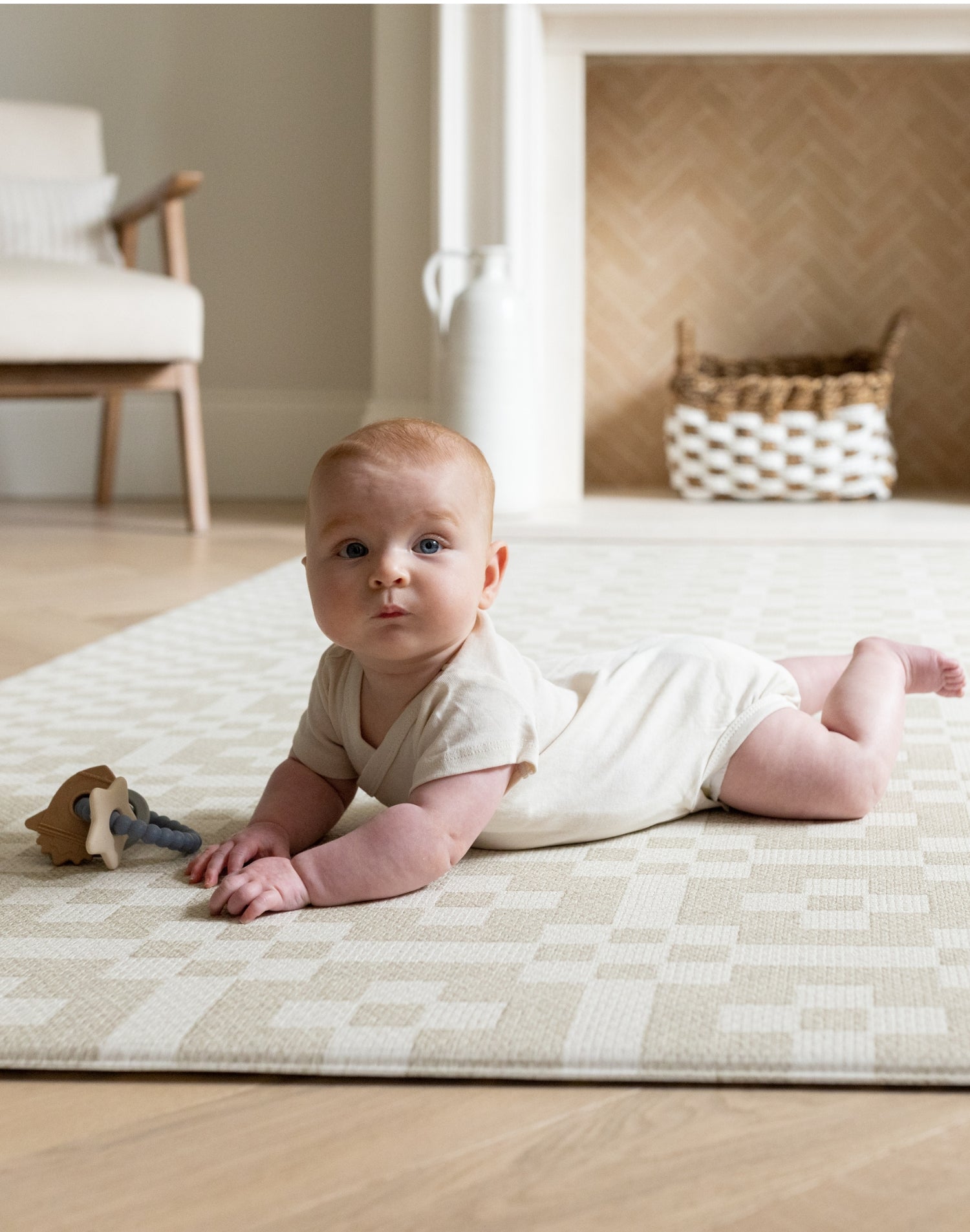 Baby on The Holbein, a calming colour playmat with a Portcullis motif in stone and chalk for tummy time and play.
