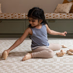 A girl plays on The Holbein, a large baby playmat for toddlers with a heritage-inspired, Welsh tapestry pattern.