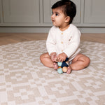 Toddler sits quietly on The Holbein, a muted beige playmat designed for comfort, play, and peaceful moments.