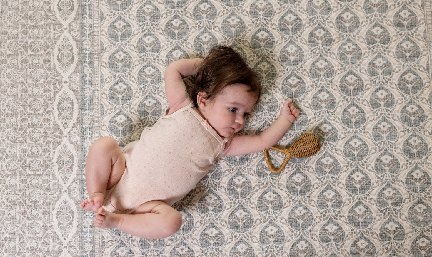 Baby lying on a patterned rug  playmat with a rattle toy