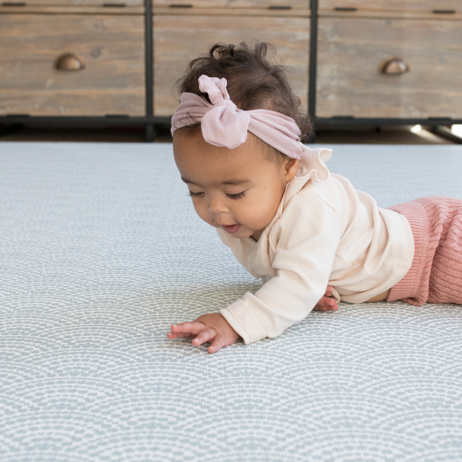 Baby lays on tummy on floor mat interested in the beautiful scalloped motif inspired by Japanese Seigaiha waves