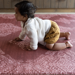 Baby crawling on deep red play mat with intricate batik inspired detailing memory foam provides support for knees and crawling babies 