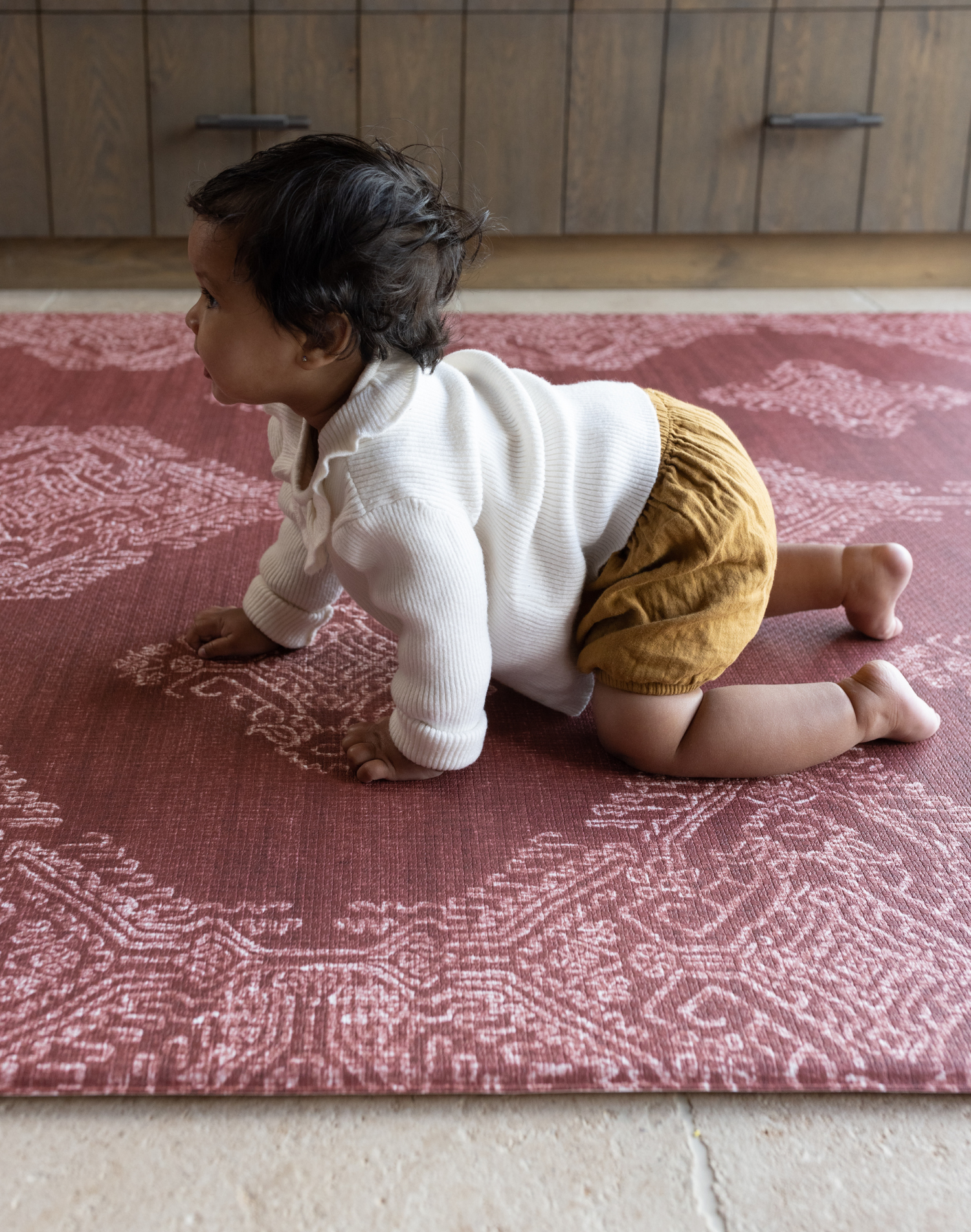 Baby crawling on deep red play mat with intricate batik inspired detailing memory foam provides support for knees and crawling babies 