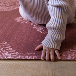 Babies hand folds across the soft edge of the Merah red play mat with supportive memory foam comfort