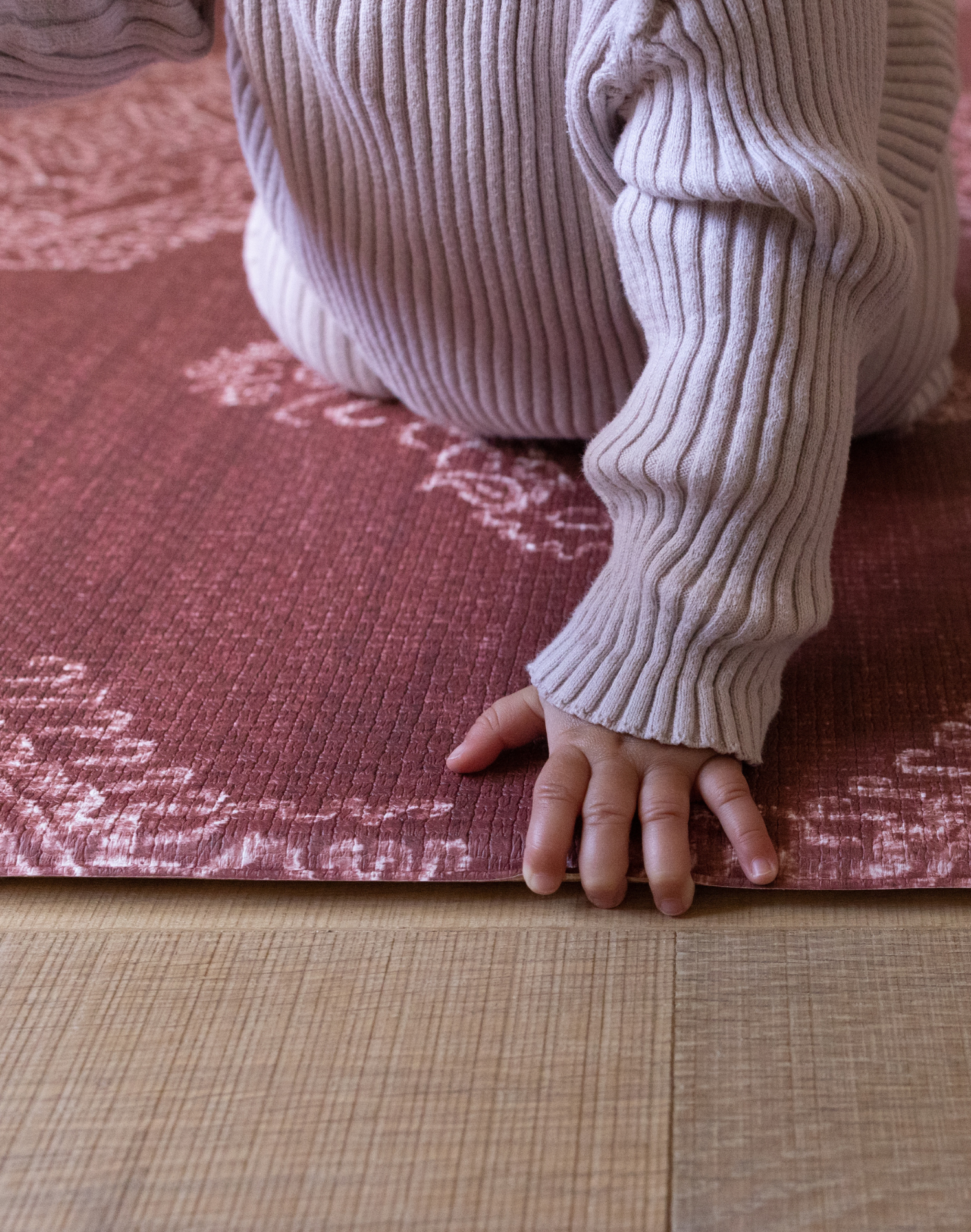 Babies hand folds across the soft edge of the Merah red play mat with supportive memory foam comfort