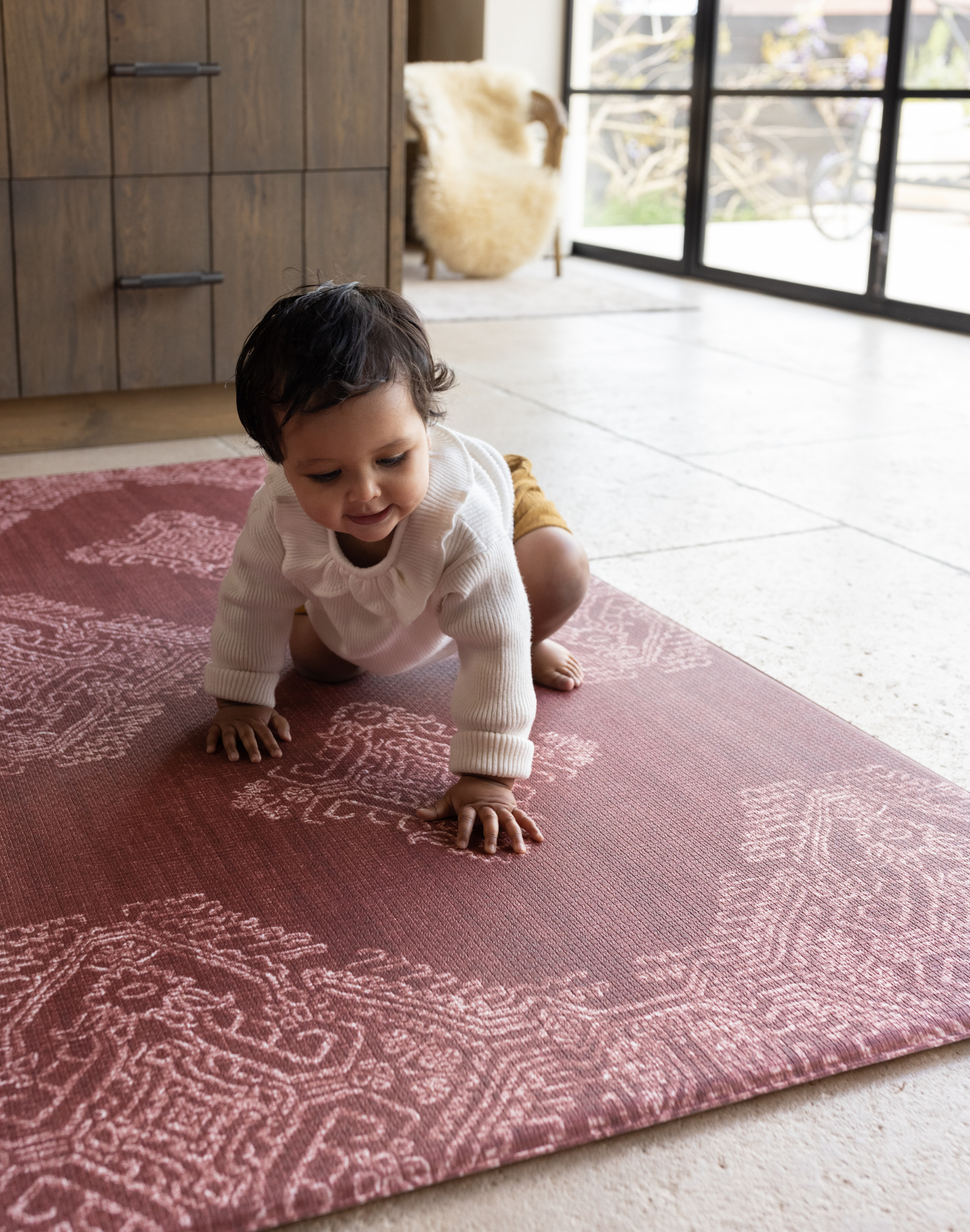 Baby crawls across red play mat the Merah with a beautiful handdrawn Batik inspired design thick memory foam protection ideal for tiled kitchen flooring