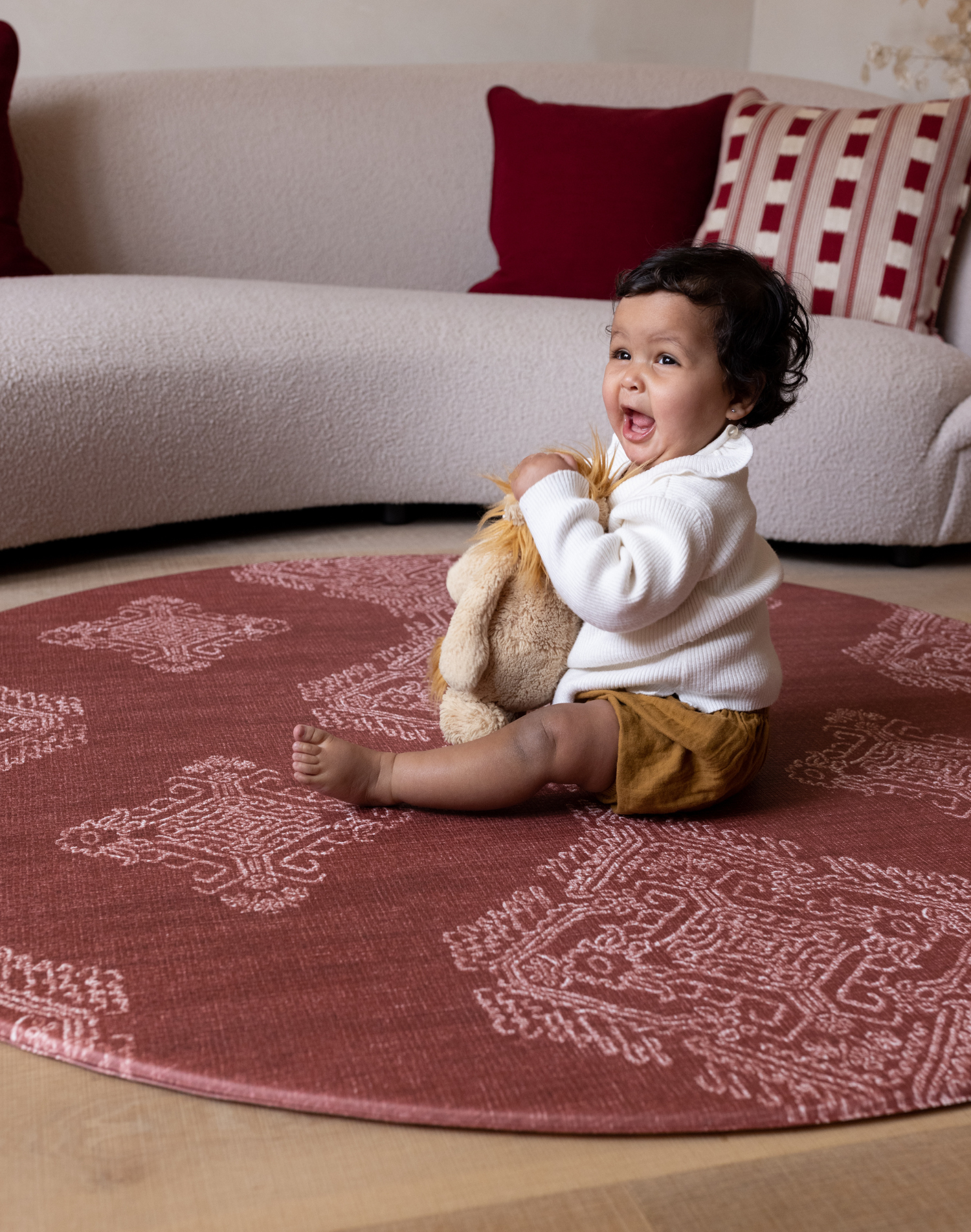 Cute baby plays with soft toy on protective red round play mat ideal for play corners in the home