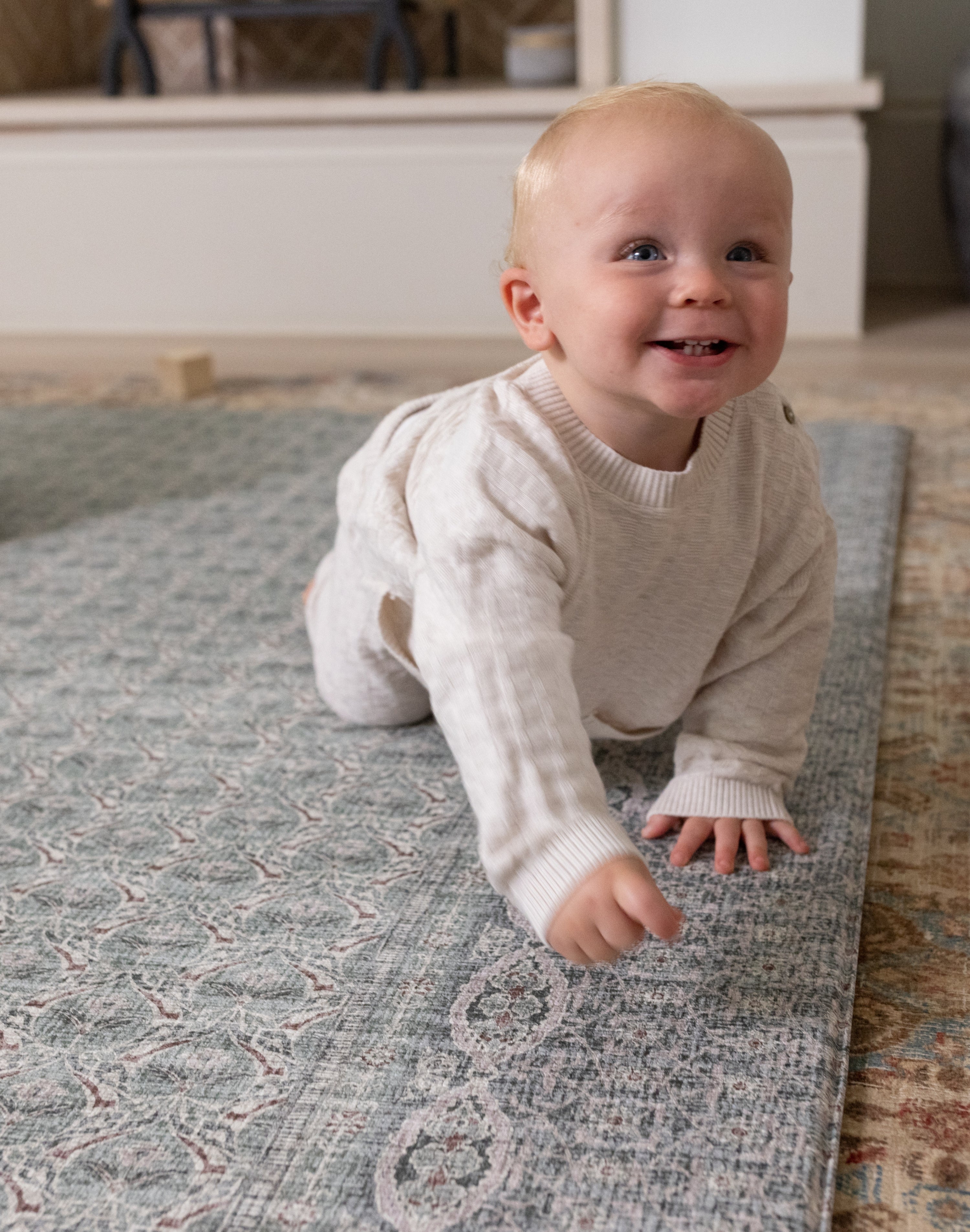 Baby crawling on a cushioned playmat with a Persian rug design