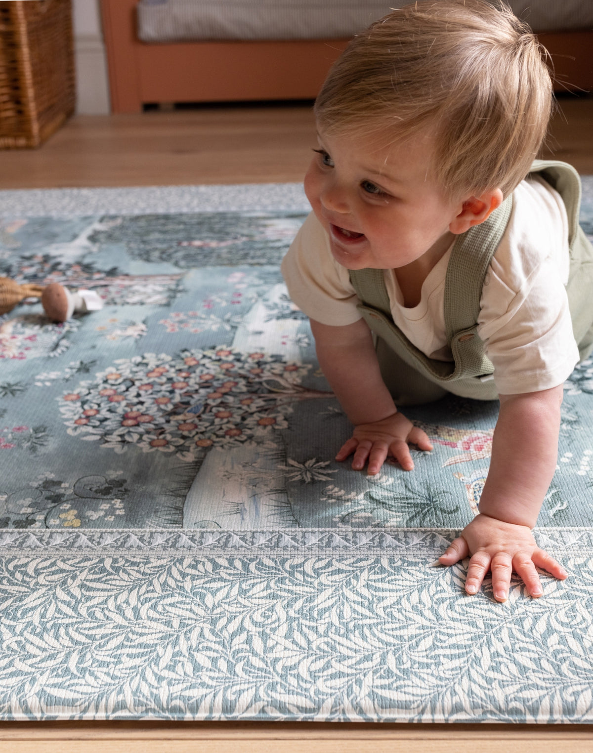 Happy toddler crawls on a Totter + Tumble luxury padded play mat in a William Morris botanical design. It is a a non-toxic, stylish addition for any modern nursery.