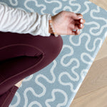 Person sitting on a blue and white patterned yoga mat on a wooden floor.