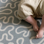 Baby's feet on a textured light blue rug with wavy patterns