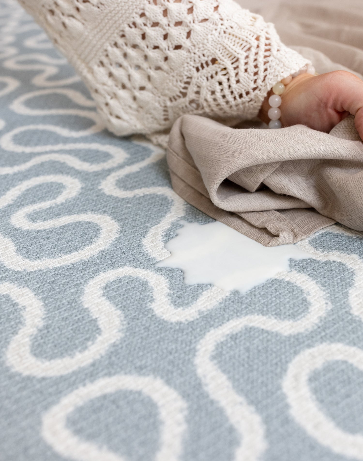 Person using a baby muslin to easily wipe clean a light blue and white patterned newborn playmat
