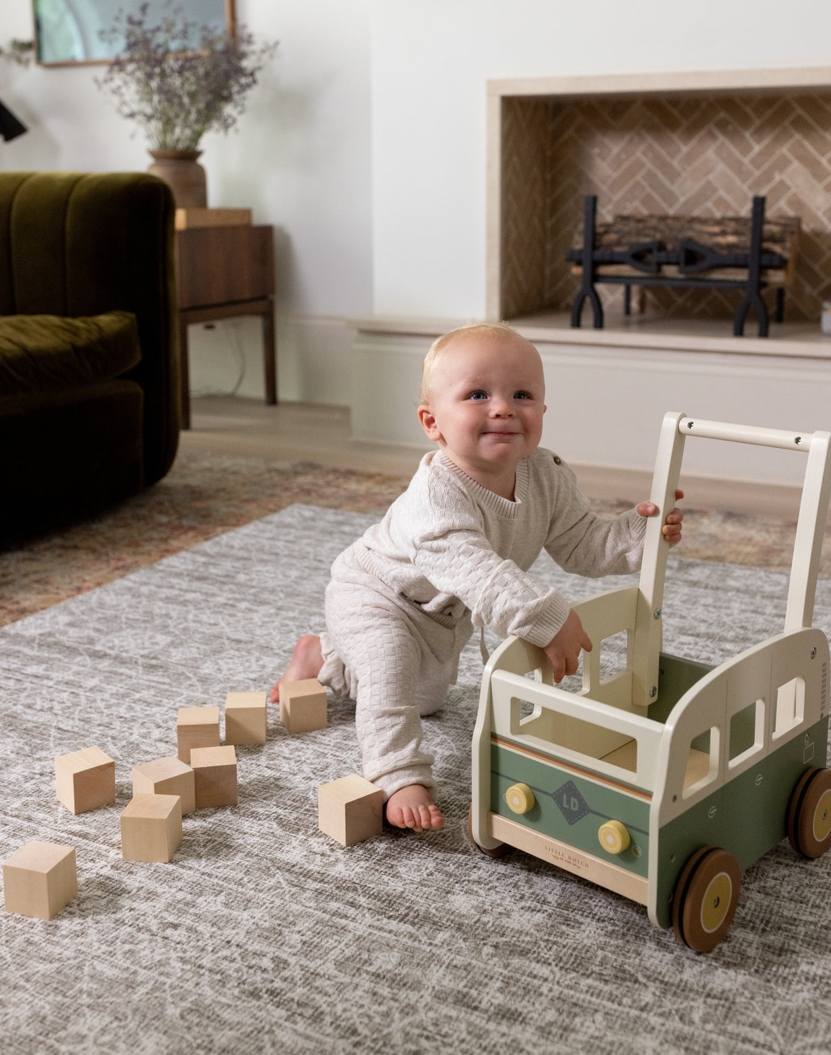 Baby playing with a wooden toy car and blocks on a Persian padded play rug in a living room.
