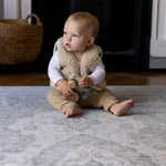 A baby sits up and is playing with a toy in the living room on a large playmat for infants