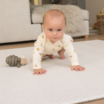 Baby crawling and playing on padded playmat with wooden toy