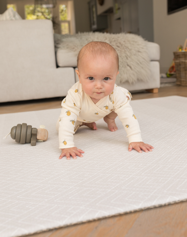 Baby crawling and playing on padded playmat with wooden toy