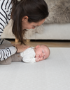 Mum rests gentle hand on the back of a baby laying on a supportive playmat with a gentle design ideal for modern spaces 