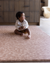 Baby sitting unaided and in comfort on the warm sand orange play mat the Rusa with a textural animal print design 