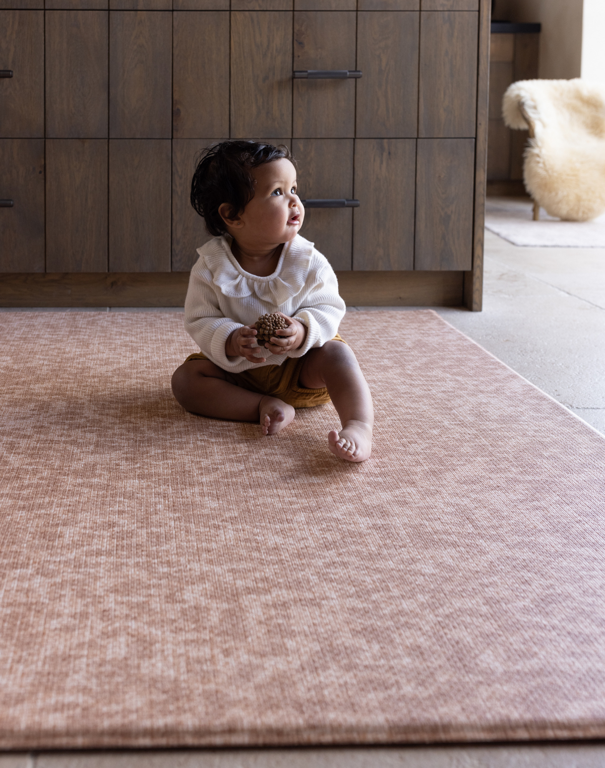 Baby sitting unaided and in comfort on the warm sand orange play mat the Rusa with a textural animal print design 