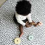 Baby plays with wooden stacking toy supported on the large round baby mat by totter and tumble