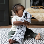 Little boy plays with crinkly book supported on the black and white Scout foam baby mat 