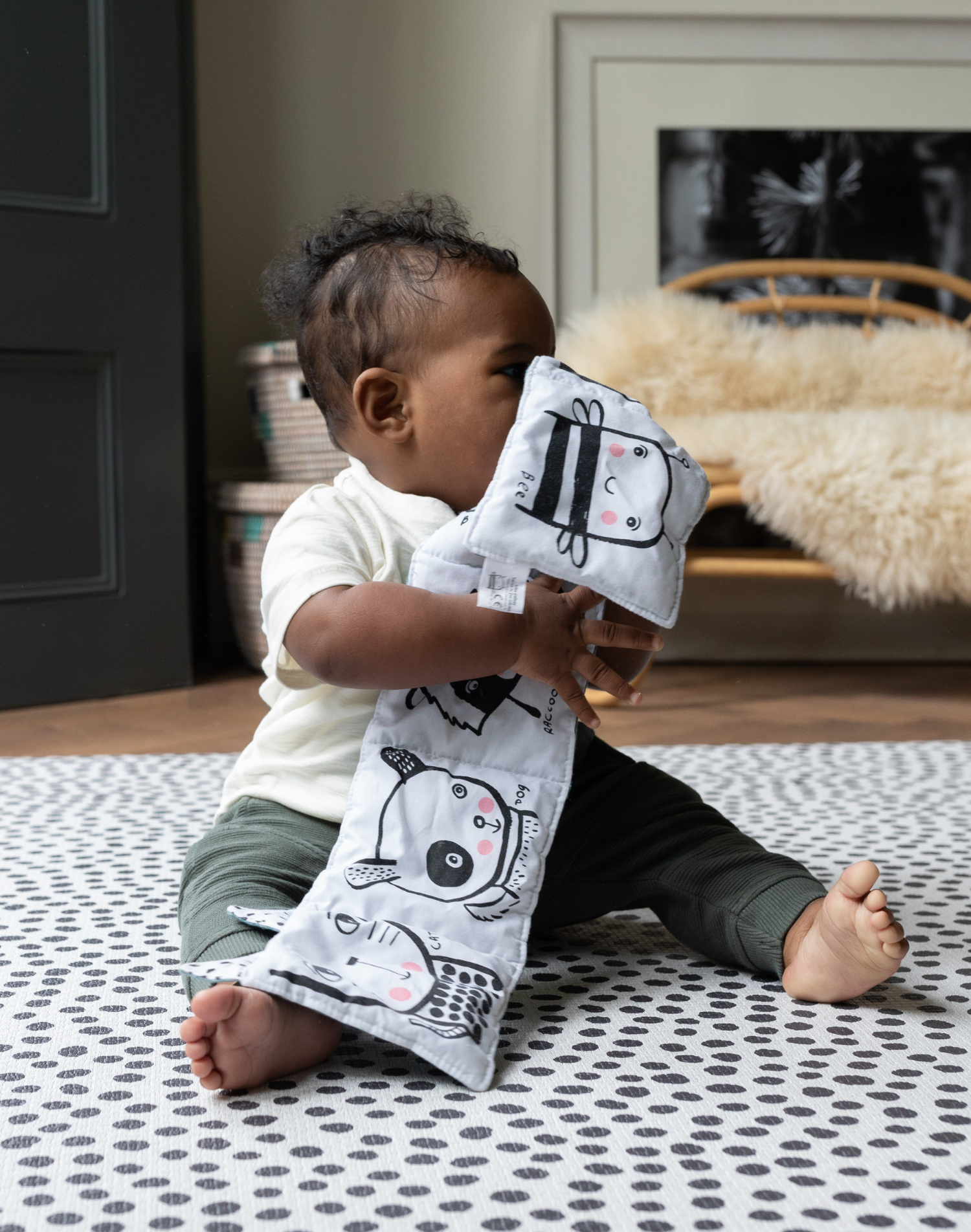 Little boy plays with crinkly book supported on the black and white Scout foam baby mat 