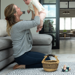 Lady holds up baby during play time on the extra large round play mat by totter and tumble with a polka dot design 