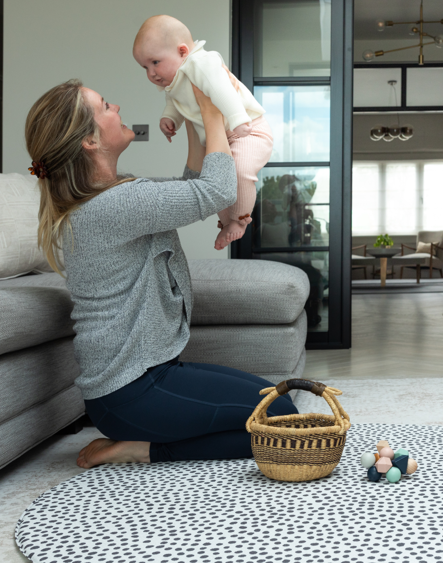 Lady holds up baby during play time on the extra large round play mat by totter and tumble with a polka dot design 