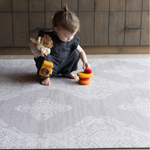 Toddler stacking smooth wooden pebbles and playing with other toys on the soft Grey play mat the Sepi with a delicate batik design that looks like a rug thick memory foam supports as she enjoys floortime