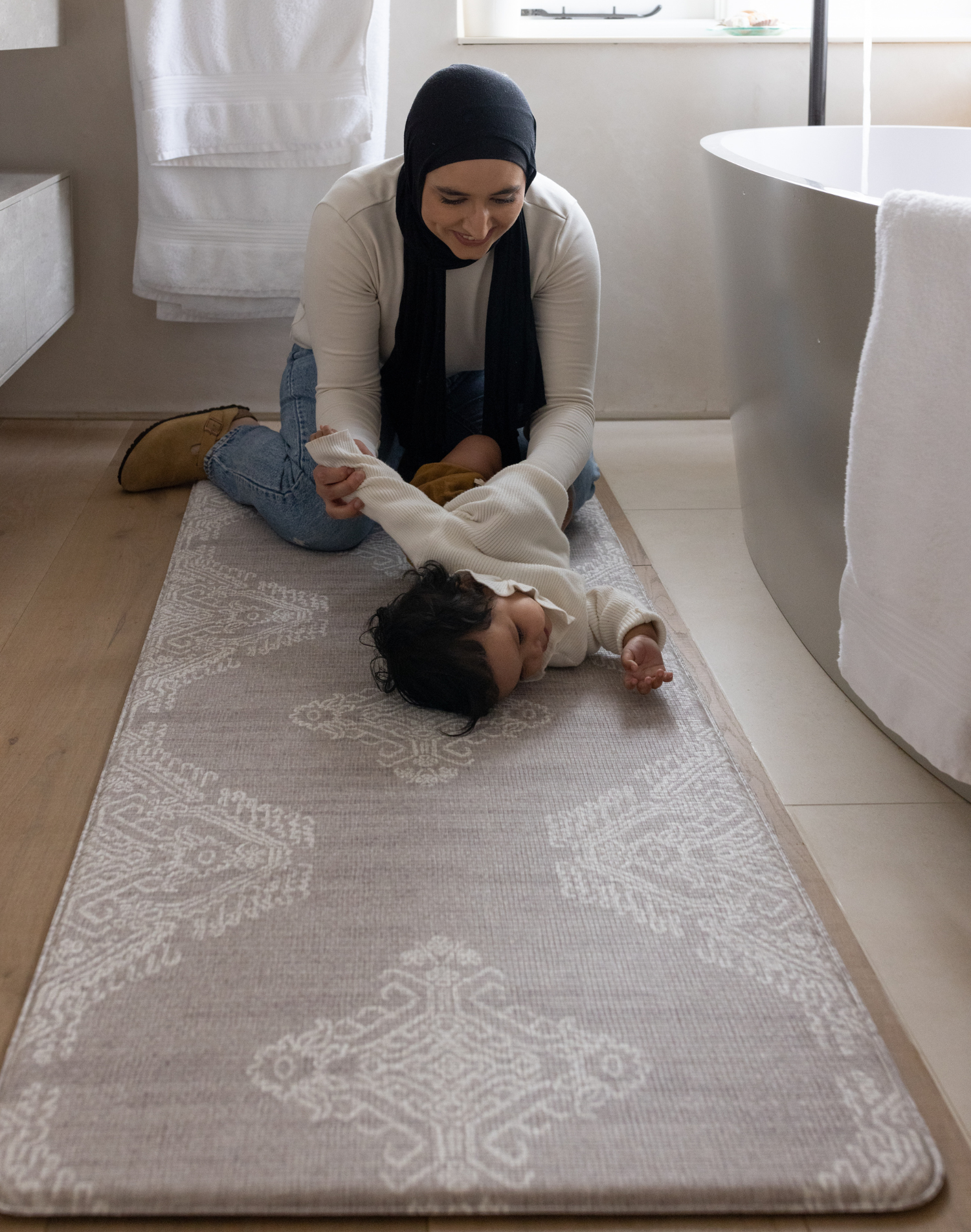 Mother changes baby girl on the large bathroom mat the sepi ideal as a kitchen mat and exercise mat in the home too with a gentle grey design to style seamlessly into modern family interiors 