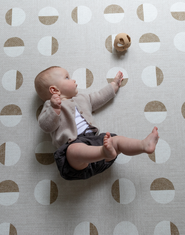 Baby rolls across beige baby playmat with subtle motif reaching for silicone baby toy 