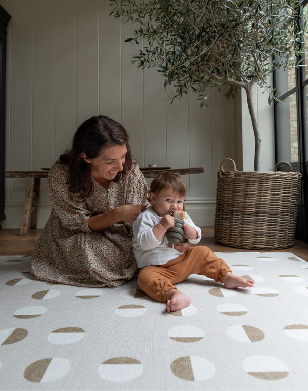 Mother and toddler enjoy play time on a greige play mat with a supportive stylish design to keep everyone comfortable on the floor 