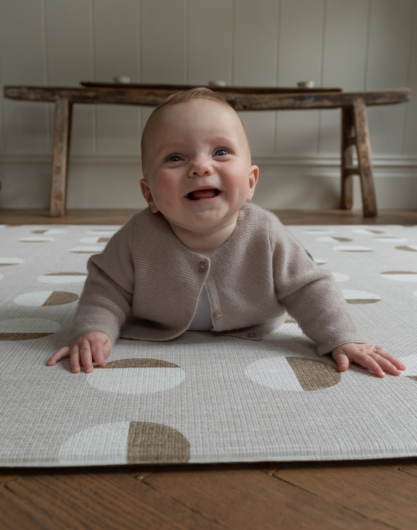 Baby is supported on thick memory foam beige play mat with a subtle motif