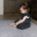 Toddler sits playing on grey leopard print play mat the sunda with a gentle jute texture background that looks stylish in modern spaces thick memory foam keeps little ones supported and protected on hard tiled and wooden flooring