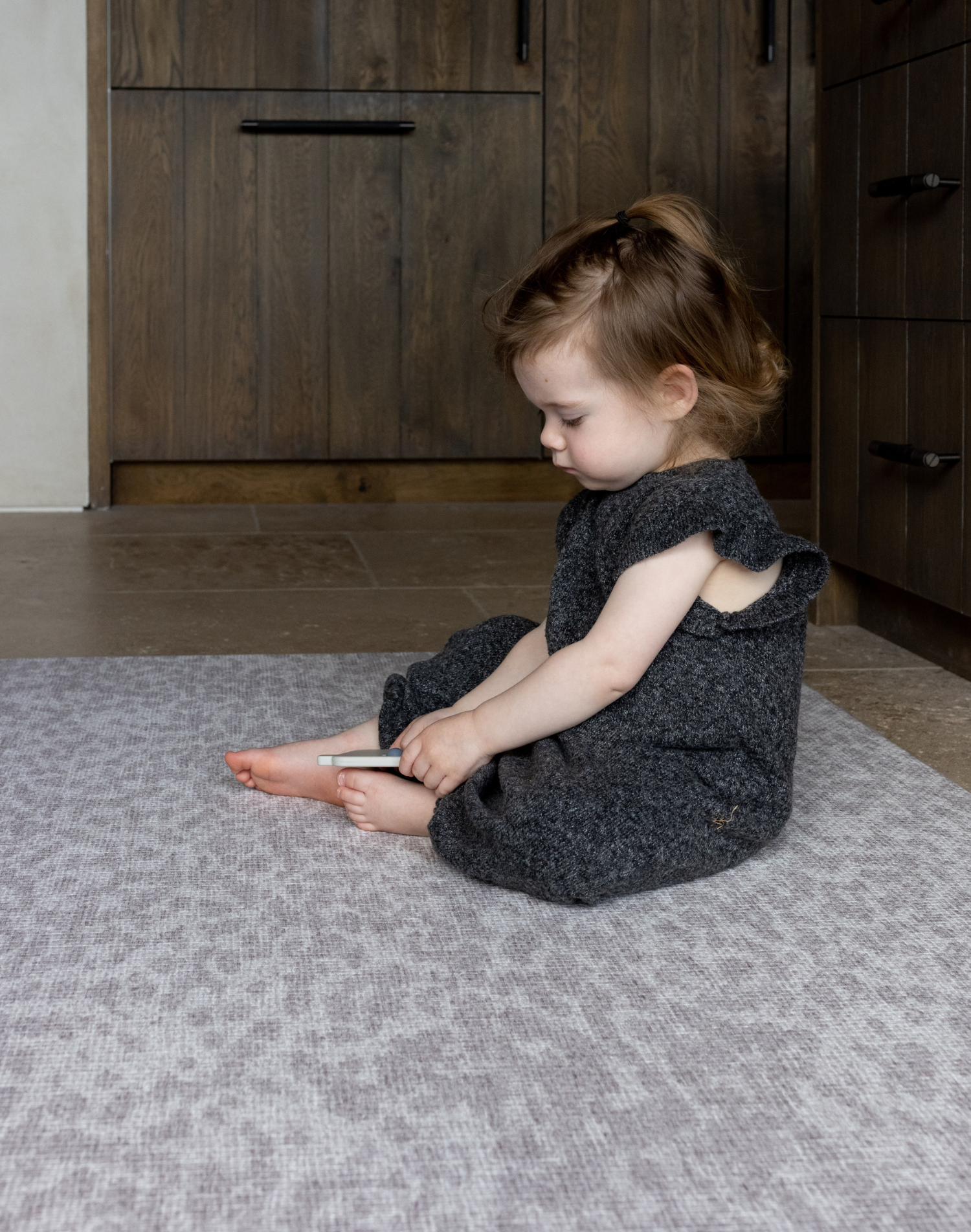 Toddler sits playing on grey leopard print play mat the sunda with a gentle jute texture background that looks stylish in modern spaces thick memory foam keeps little ones supported and protected on hard tiled and wooden flooring