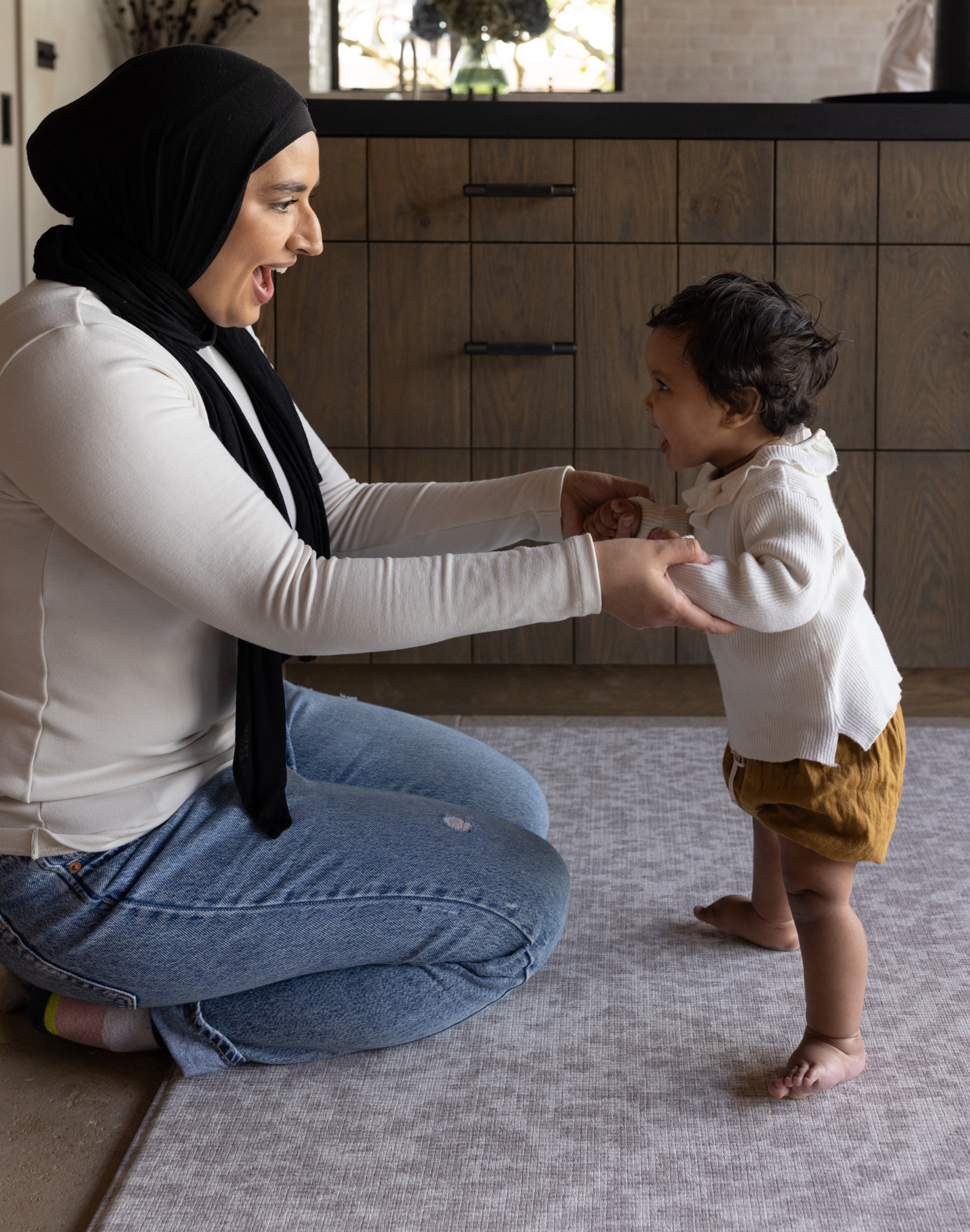 Baby girl stands on memory foam play mat supported by mother protective memory foam keeps baby and mother comfortable during play time and milestone development