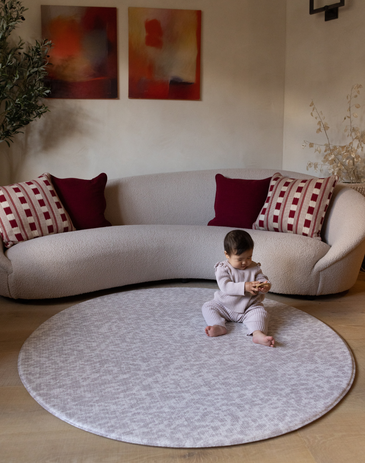 Baby girl plays with toy sitting on animal print play mat in light grey tone small round play mat size is ideal for placing in front of sofa for safe play in the family home