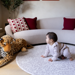 Baby crawls on grey leopard print playmat providing support on the floor during play time with a large soft leopard toy 