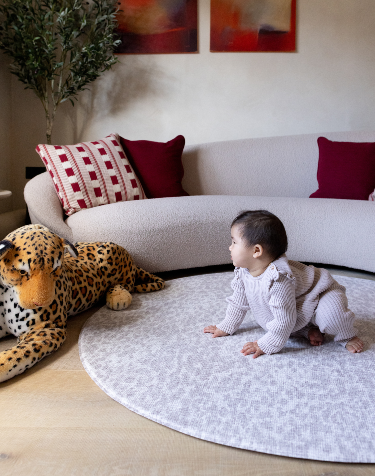 Baby crawls on grey leopard print playmat providing support on the floor during play time with a large soft leopard toy 