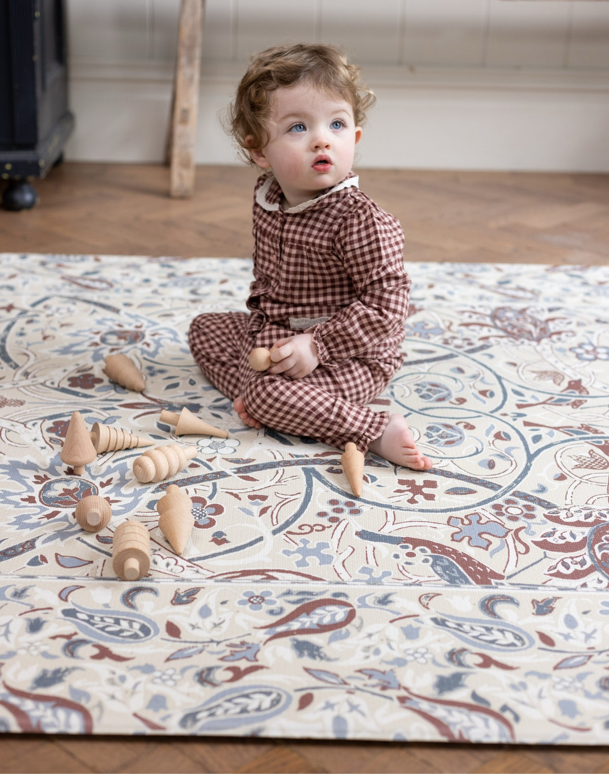 Child playing with wooden toys on a Bullerswood design William Morris x Totter and tumble padded play mat collaboration