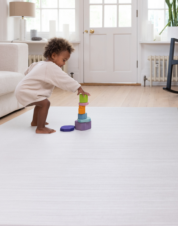 Toddler stacking wooden toys on Baby play mat with modern tan and beige gradient motif 