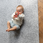 Baby plays with non toxic teething toy laying on comfortable play mat that keeps little ones off cold hard floors 